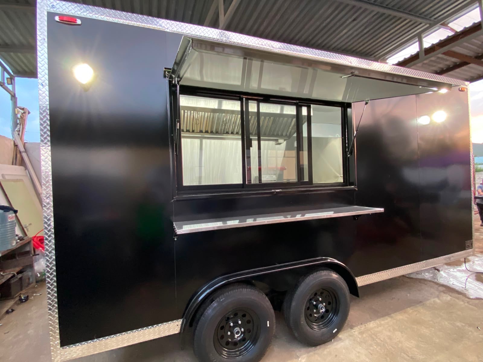 Black custom food truck in the shop with the awning window open, sliding glass panels and a fold-down stainless service counter.