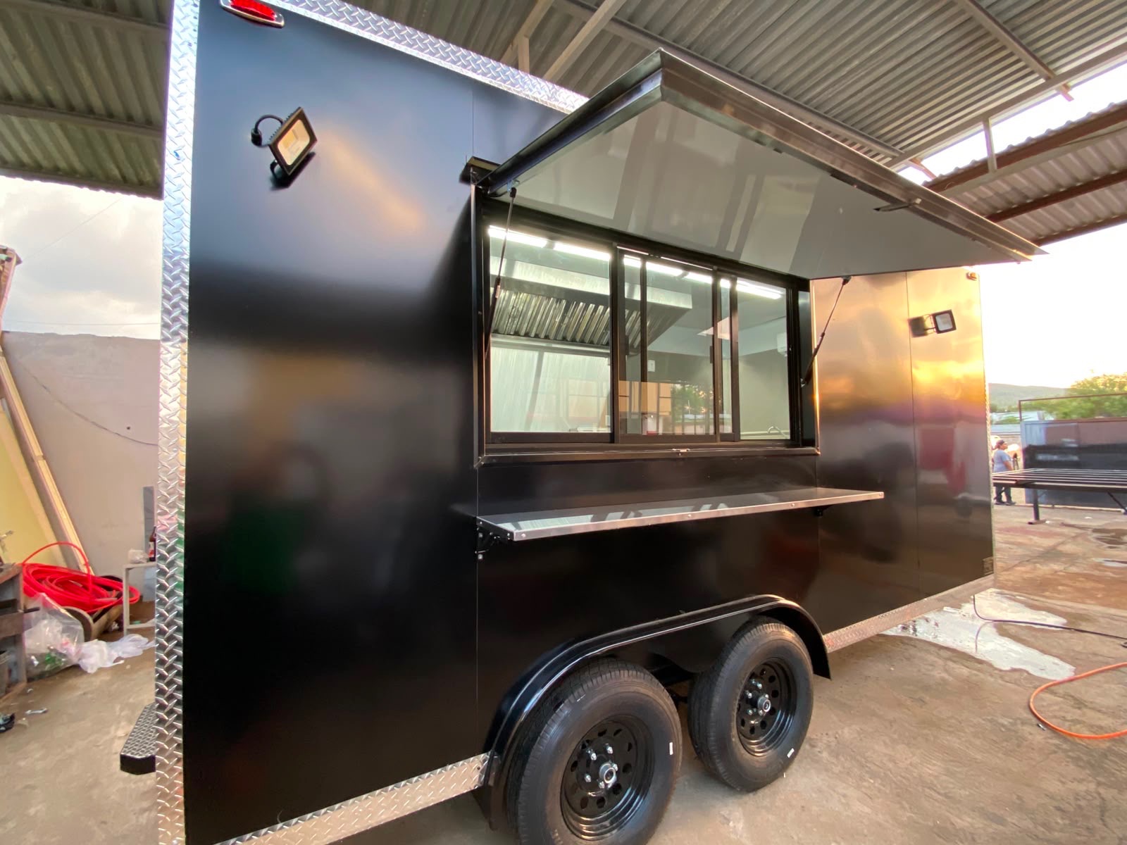 Black food truck with the awning window open, stainless service counter and interior lighting on.
