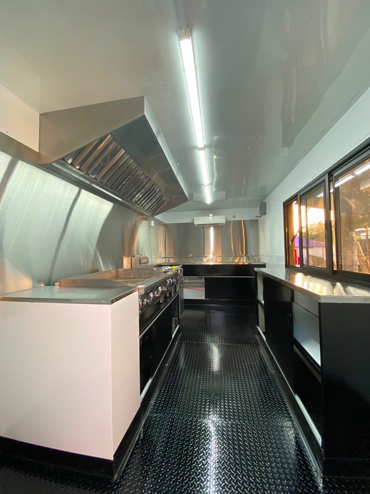 Interior of the food truck looking down the galley: stainless hood, cook line and diamond-plate floor.