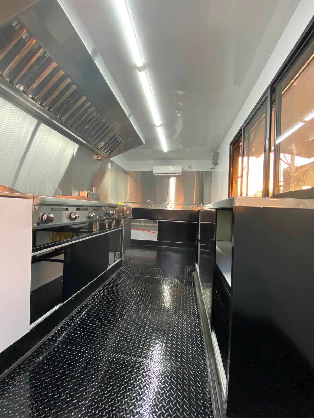 Cook line with range and flat-top griddle under the extraction hood, with a wall-mounted air conditioner at the far end.