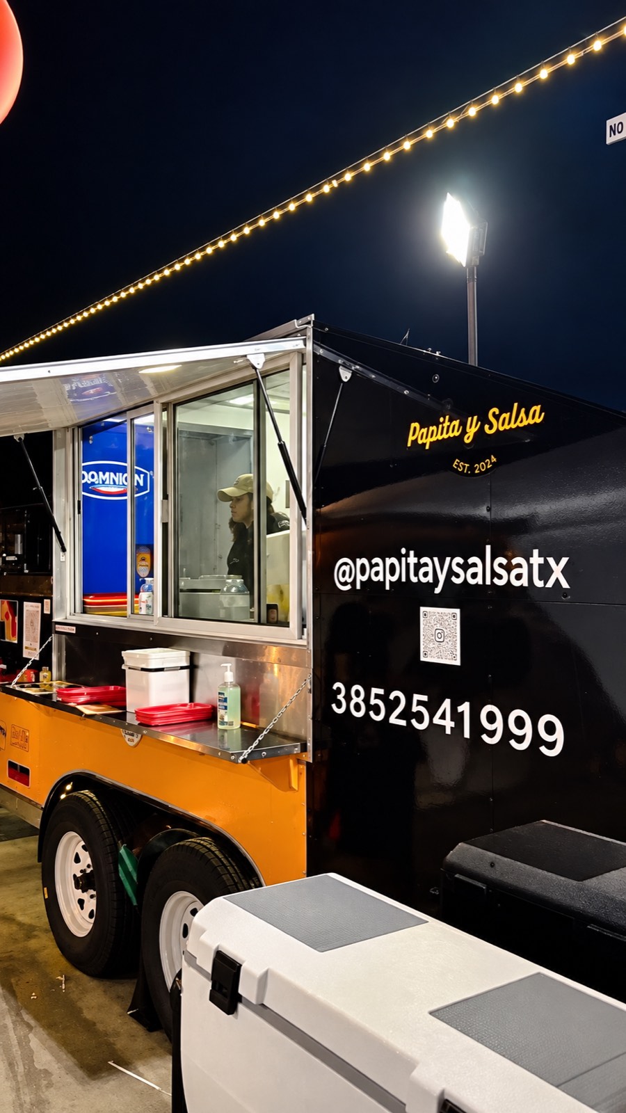 Papita y Salsa food truck serving after dark, the galley lit inside and the service window open under string lights.