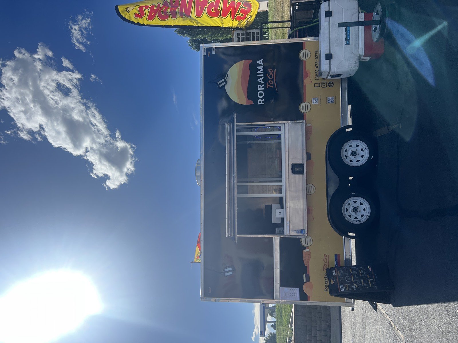 Roraima To Go food truck parked outside on a sunny day, gloss black body with the sunset logo and the awning service window propped open.