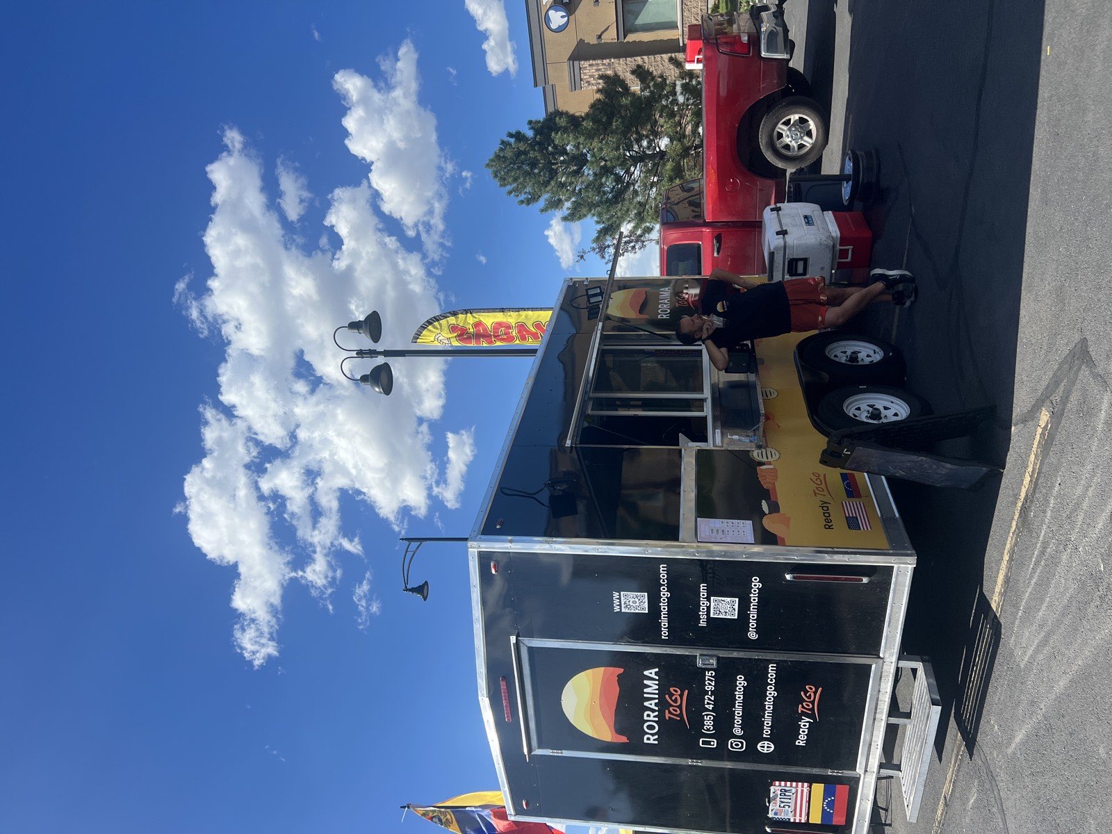 Rear three-quarter view of the Roraima To Go food truck on a service day, with the operator standing alongside it.